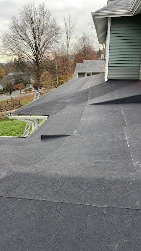 A roof of a house with a black roof and trees in the background.