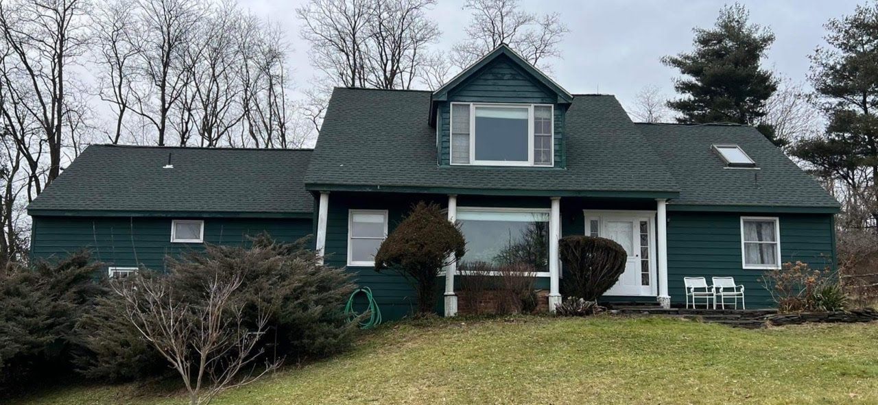 A large green house with a green roof is sitting on top of a grassy hill.