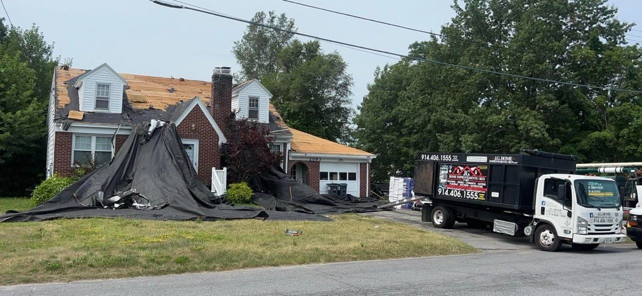 A dump truck is parked in front of a house that has a roof being repaired.