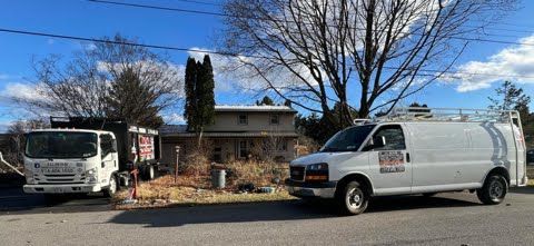Two vans are parked on the side of the road in front of a house.