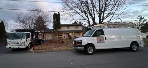 Two vans are parked on the side of the road in front of a house.