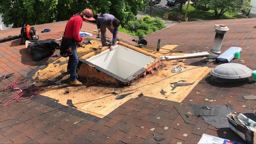 Two men are working on a roof with a skylight.