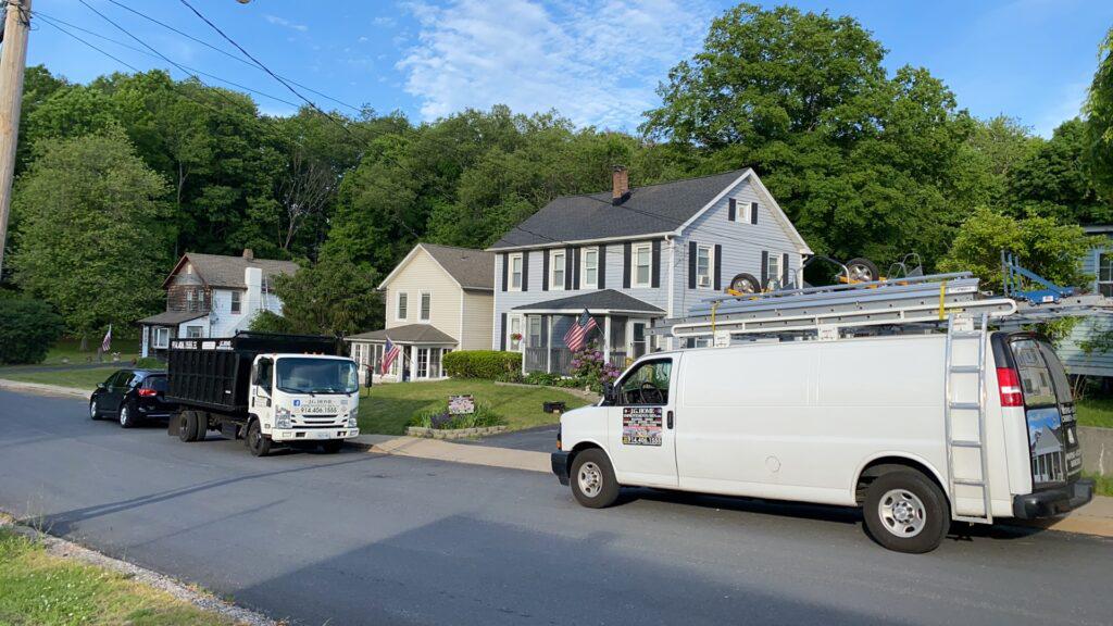 Two white vans are parked on the side of the road in front of a house.
