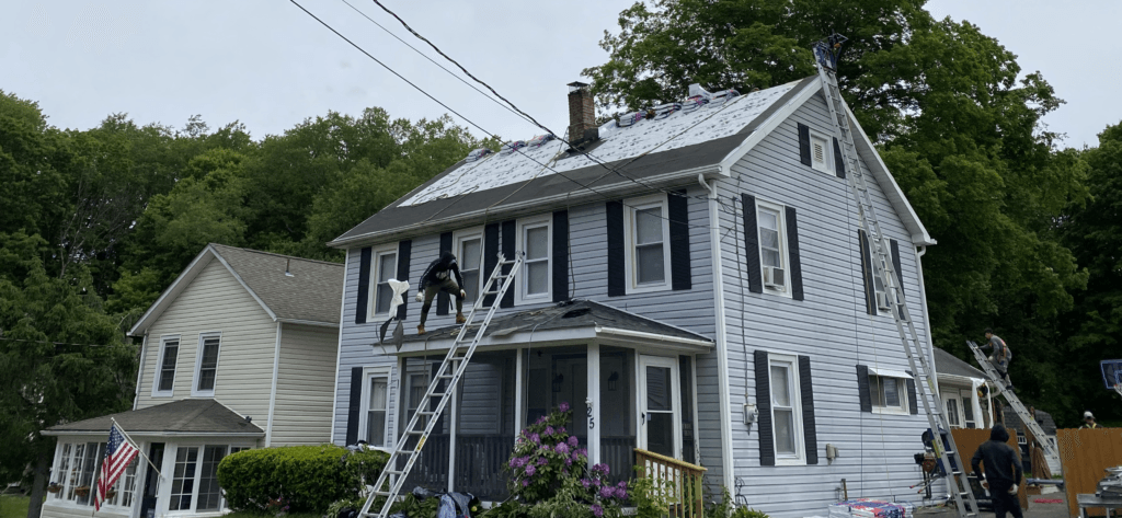 A large white house with a roof that is being painted.