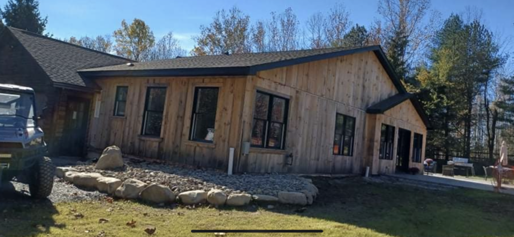 A large wooden house with a lot of windows is surrounded by trees.