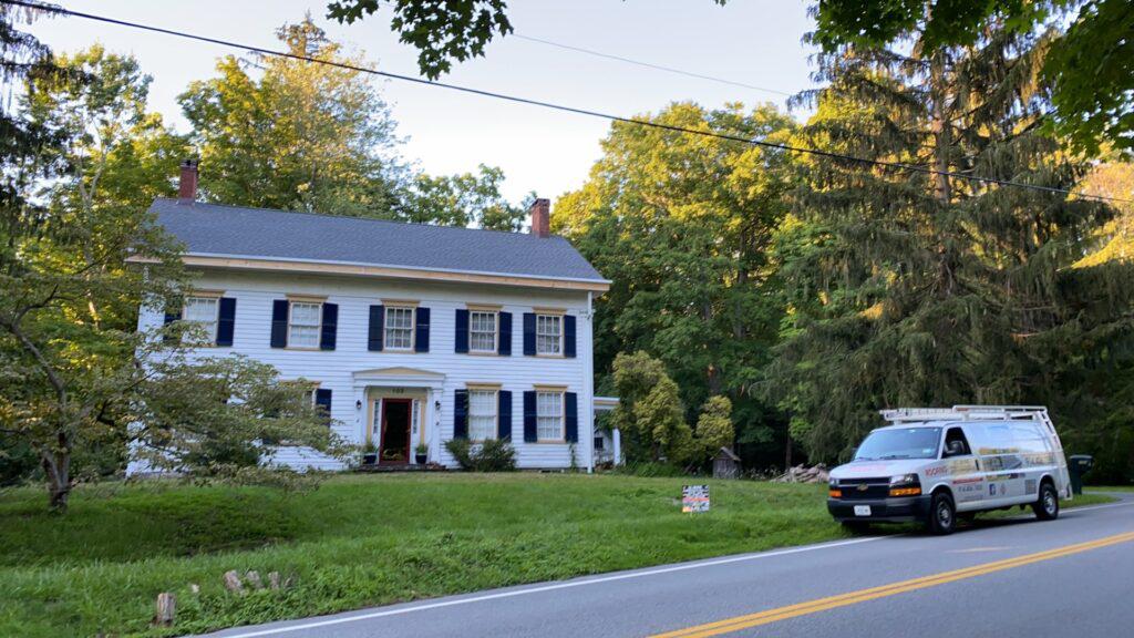 A white van is parked in front of a large white house.