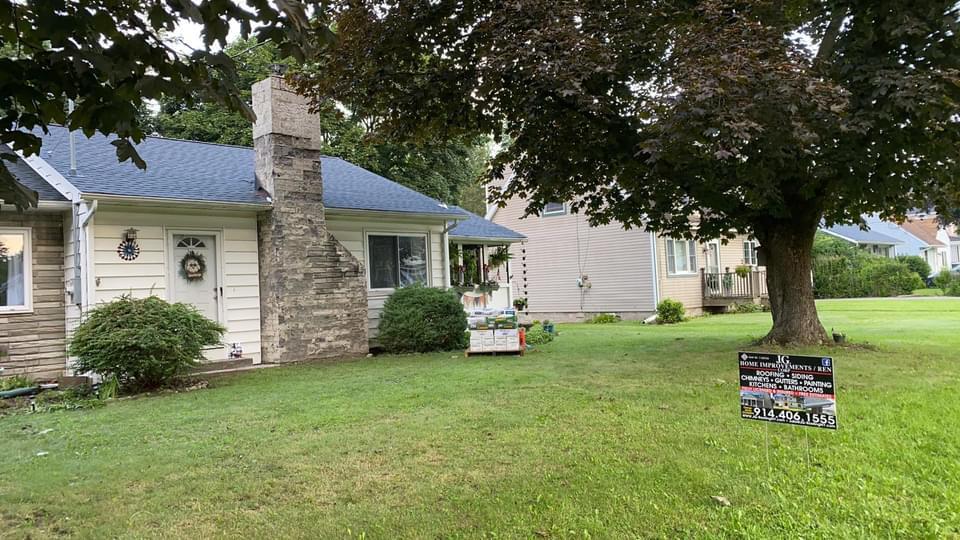 A white house with a blue roof and a sign in front of it.