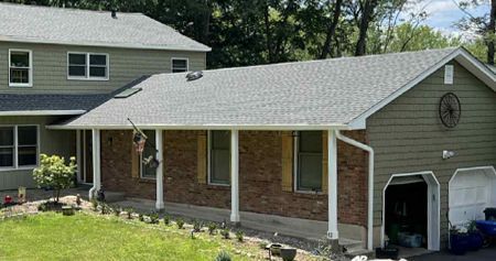 Green house with a grey roof, brick facade, and a two-car garage.