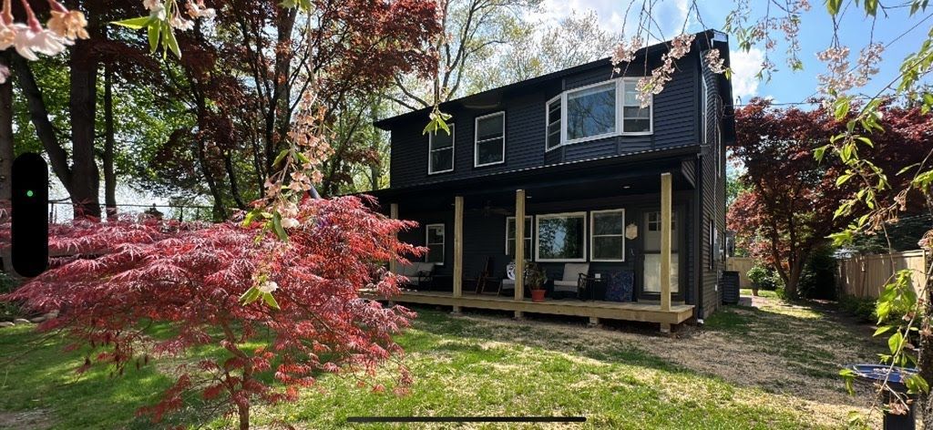 A black house with a porch and trees in front of it.