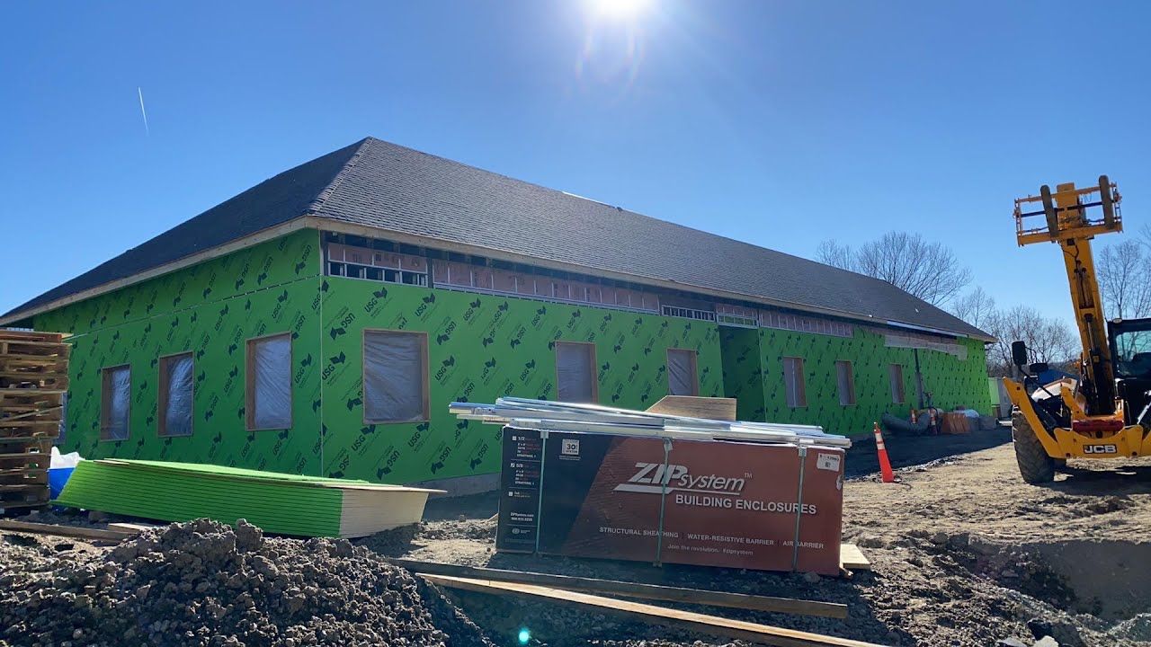 A building under construction with green insulation and a forklift in front of it.