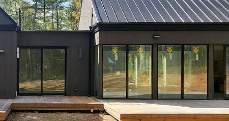 Modern dark brown building with large glass doors and a metal roof. A wooden deck is in the foreground.
