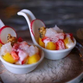 Due cucchiai da degustazione in ceramica riempiti con un'insalata di frutta fresca e frutti di mare, guarnita con una sottile fetta di ravanello.