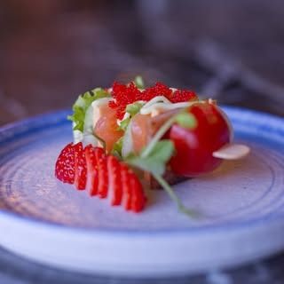 Un antipasto creativo servito su un piatto con il bordo blu, con fragole a fette, salmone, verdure e uno spiedino di pomodorini.