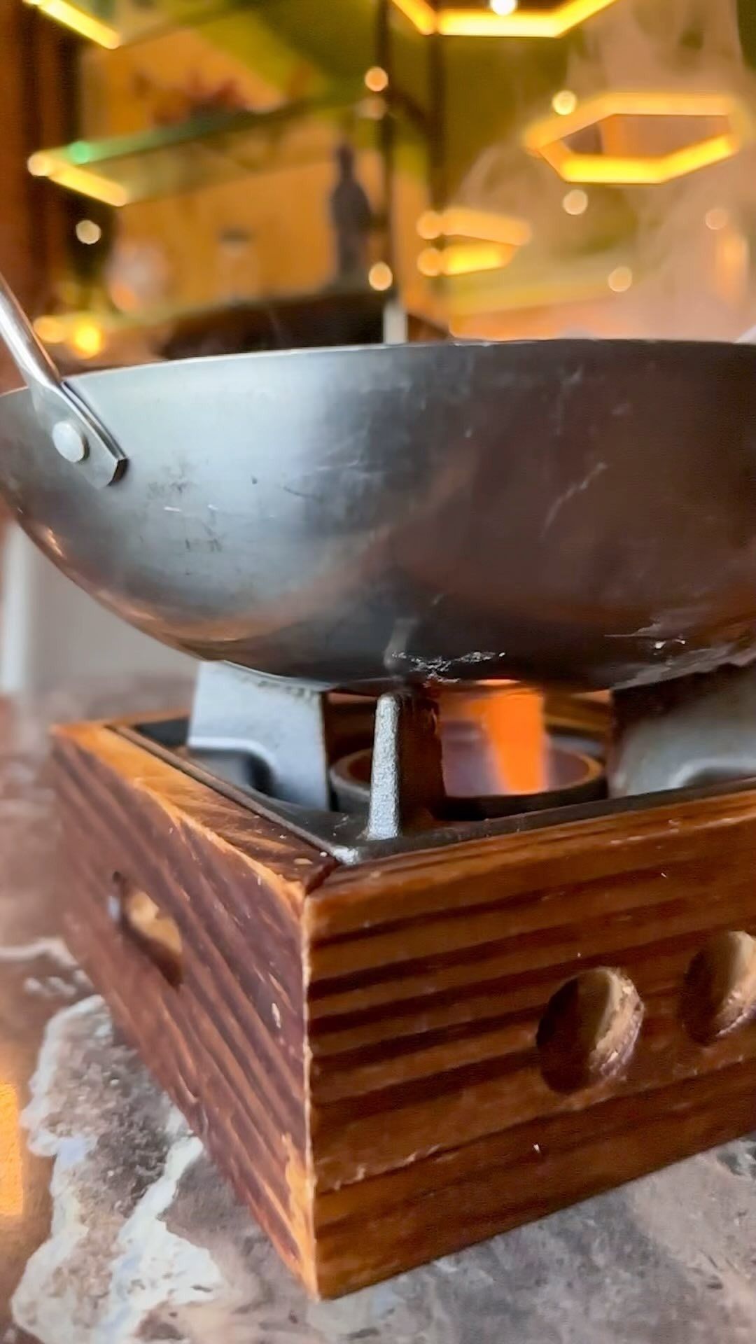 In un ristorante con luci soffuse, una piccola pentola di ferro poggia su un supporto di legno, riscaldata da una fiamma visibile.