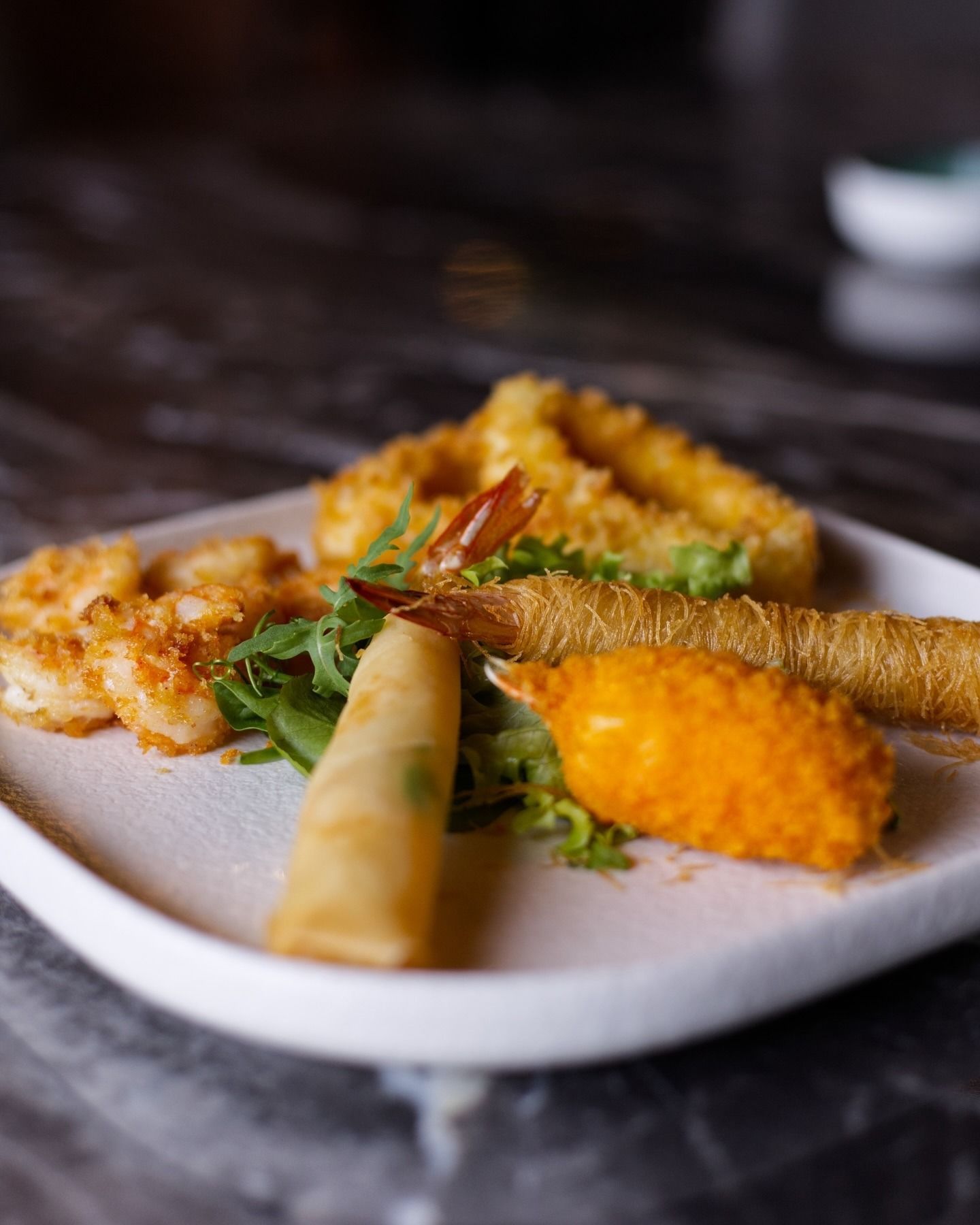 Un piatto misto di antipasti fritti, tra cui gamberi impanati, involtini primavera e chele di granchio su un letto di verdure.