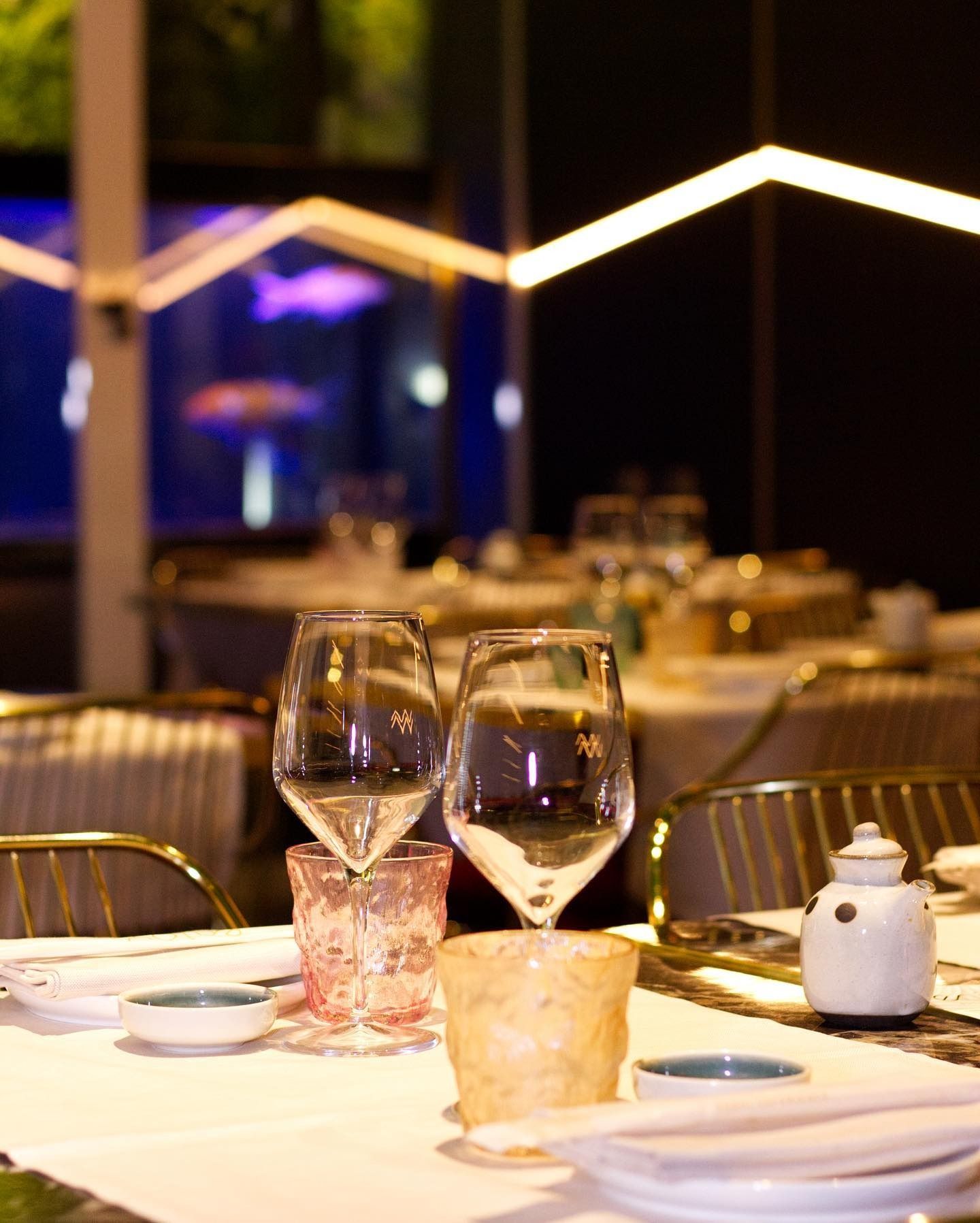 Primo piano di un tavolo da ristorante con calici da vino, bicchieri decorati, ciotoline e un barattolo di ceramica.