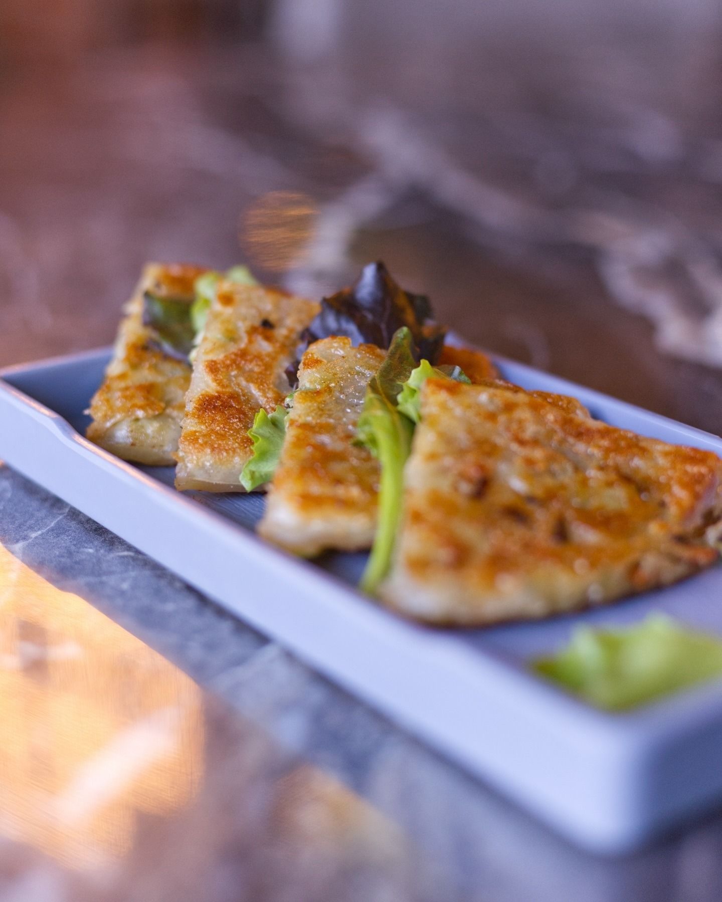 Triangoli dorati e croccanti, fritti in padella e serviti su un lungo piatto rettangolare blu, con piccole guarnizioni di lattuga verde.