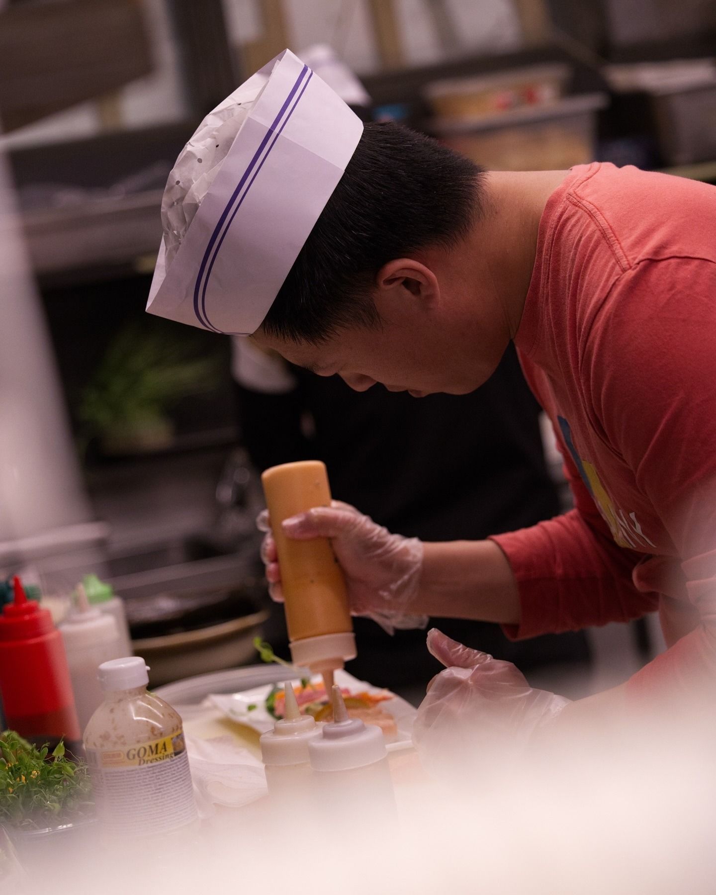 In una cucina professionale, una persona con cappello e guanti da chef spreme la salsa da una bottiglia sul cibo.