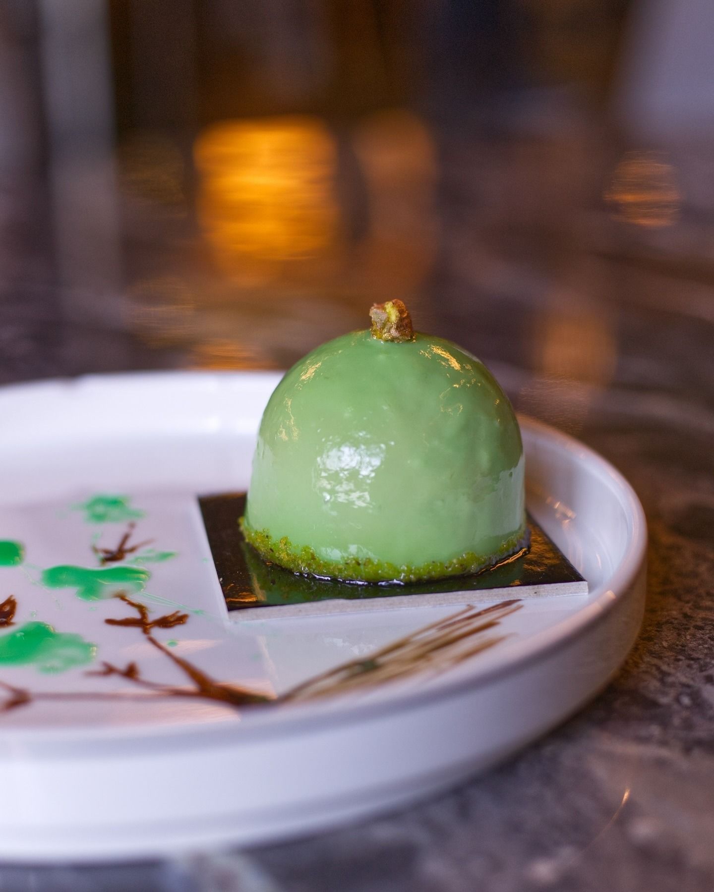 Un dolce a forma di cupola di colore verde pallido, ricoperto da una foglia d'oro e servito su un piatto decorato con motivi artistici dipinti.