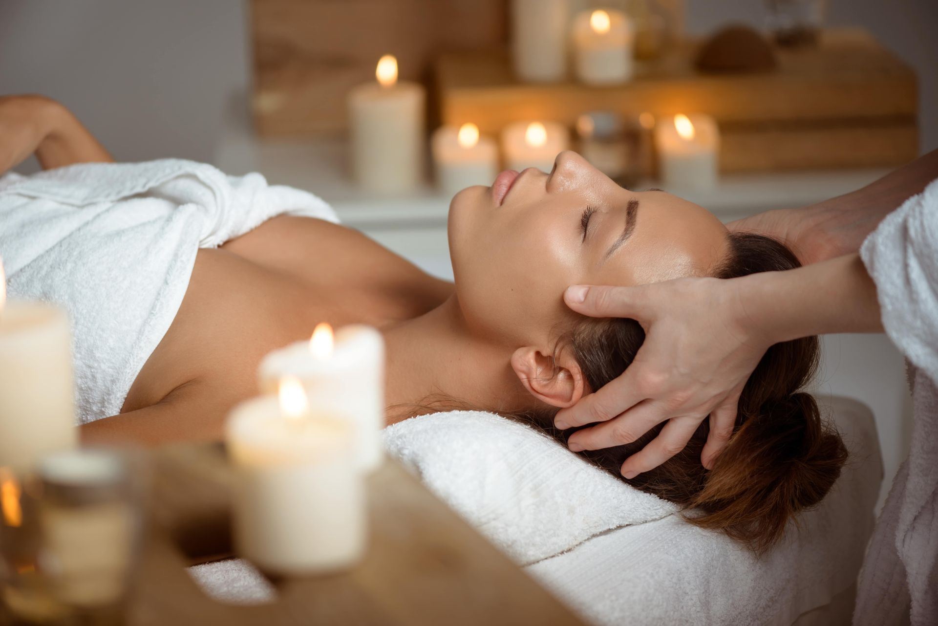 Une femme reçoit un massage de la tête dans un spa entourée de bougies.