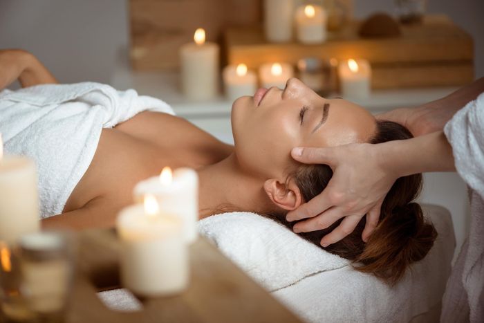 Une femme reçoit un massage de la tête dans un spa entourée de bougies.