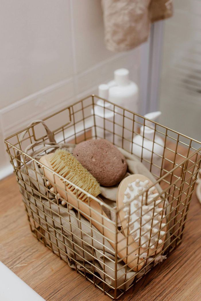 Un panier métallique rempli de brosses et d'éponges est posé sur une table en bois.