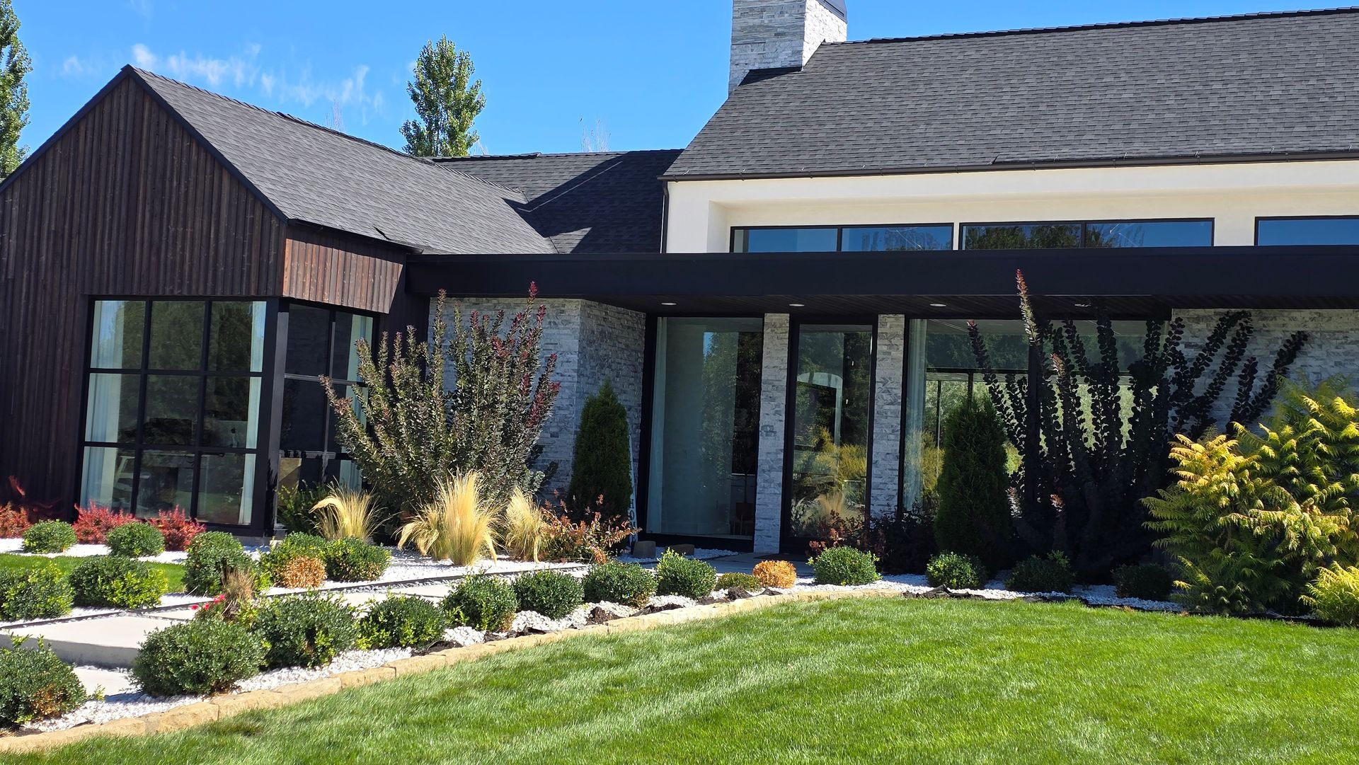 Modern home exterior with dark wood siding, stone accents, and manicured landscaping.