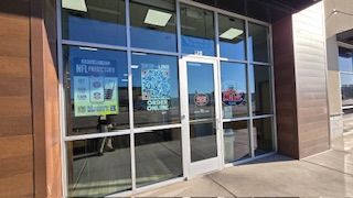 Exterior of a business with large glass windows and doors. Signage promotes online games. A person stands near the door.