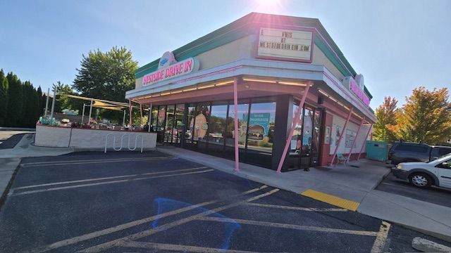 Exterior of a pink and green diner with a drive-in window under a sunny sky.