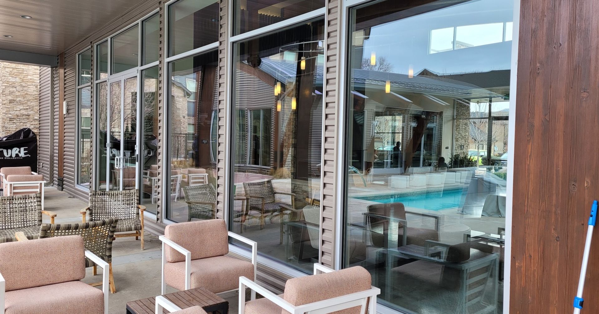 Outdoor patio with seating and large glass windows reflecting a pool and interior space.