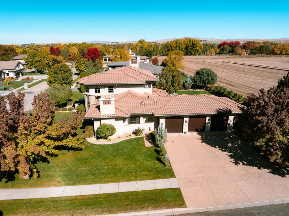 Aerial view of a two-story home with a terracotta tile roof, surrounded by a green lawn and autumn trees.