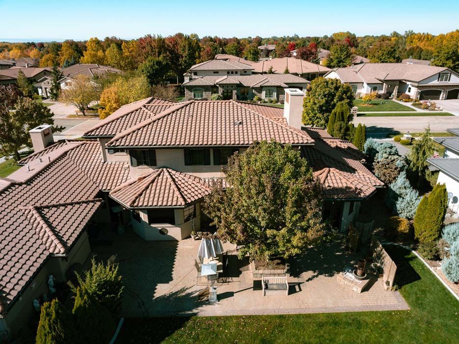 Aerial view of a large house with a terracotta tile roof and patio in a suburban neighborhood.