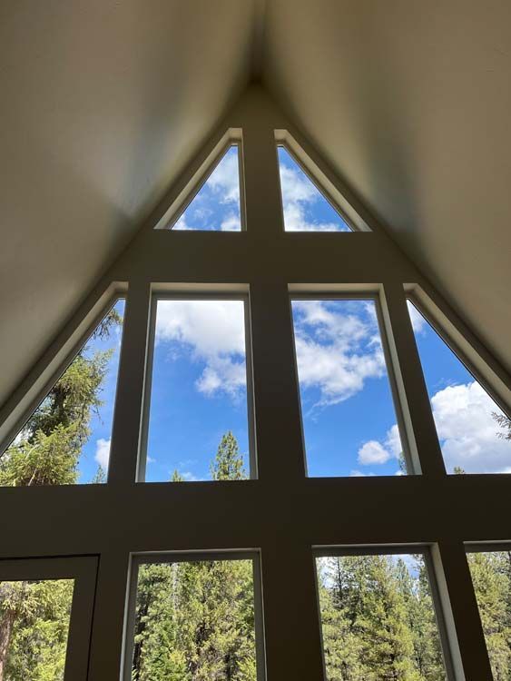 Triangular window framing a bright blue sky with fluffy clouds, overlooking green trees.