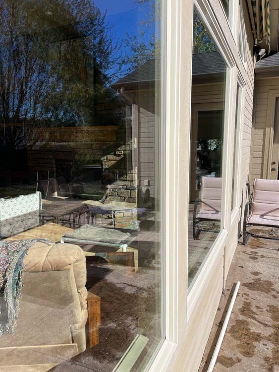 Exterior window of a house with visible outdoor furniture and reflections of the yard. Sunny day.