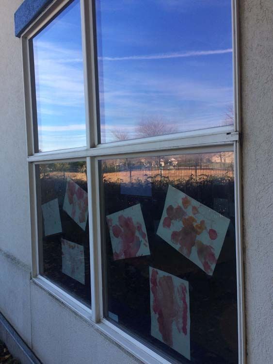 Window with children's artwork; handprints on paper. Blue sky reflected in the window.