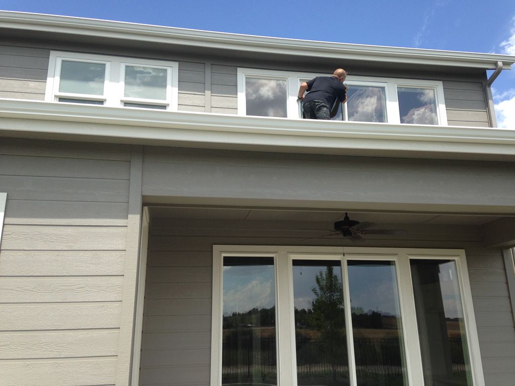 Person cleaning upper story windows of a gray house on a sunny day.