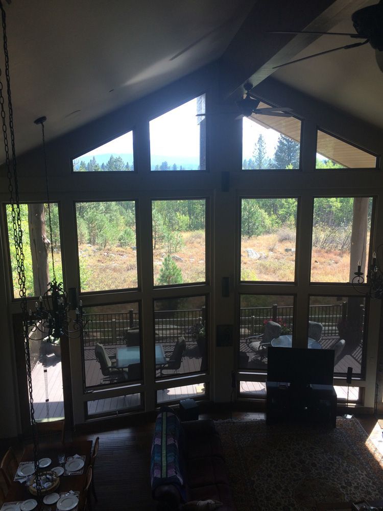 A-framed room with large windows overlooking a forest and deck. Sunlight streams in.
