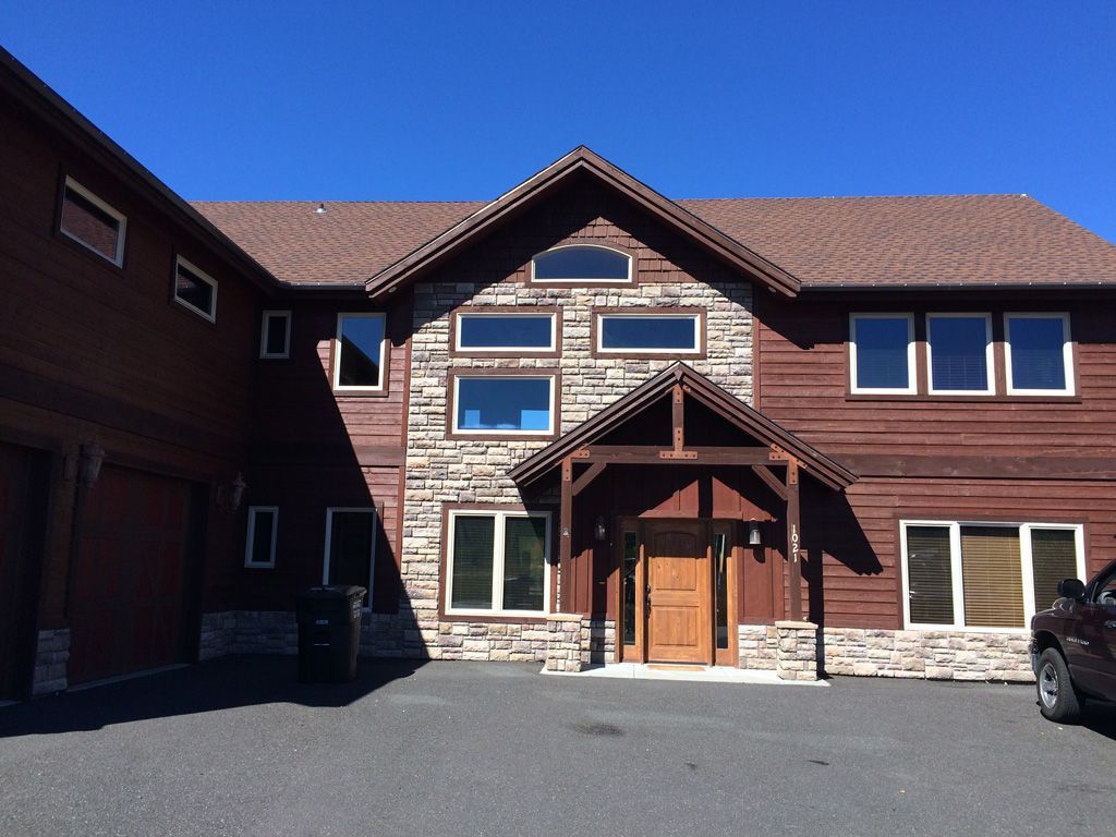 Brown wooden house with stone accents, arched windows, and brown roof under a blue sky.