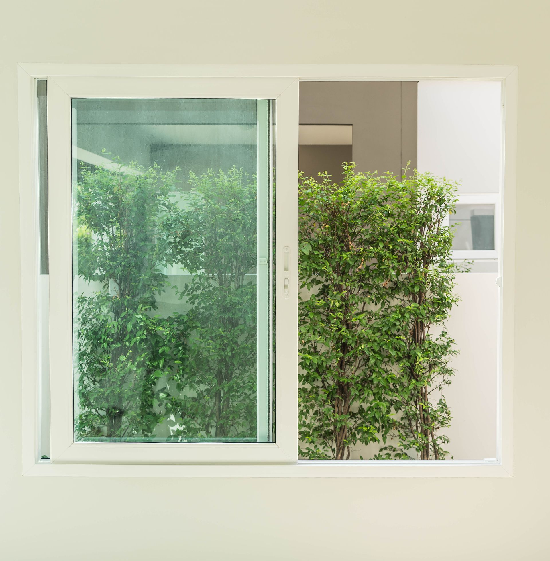 White sliding window with view of green trees and bushes outside.