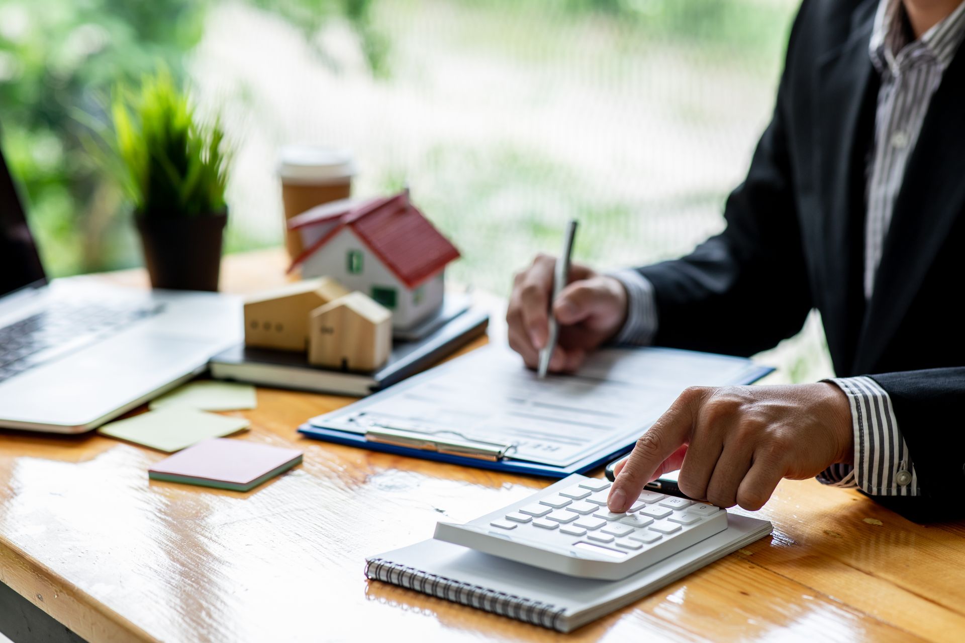 Person using a calculator, reviewing documents with small house models on a desk.