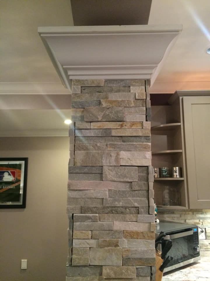 Stone-covered support column with white crown molding. Kitchen setting with cabinets and artwork visible.