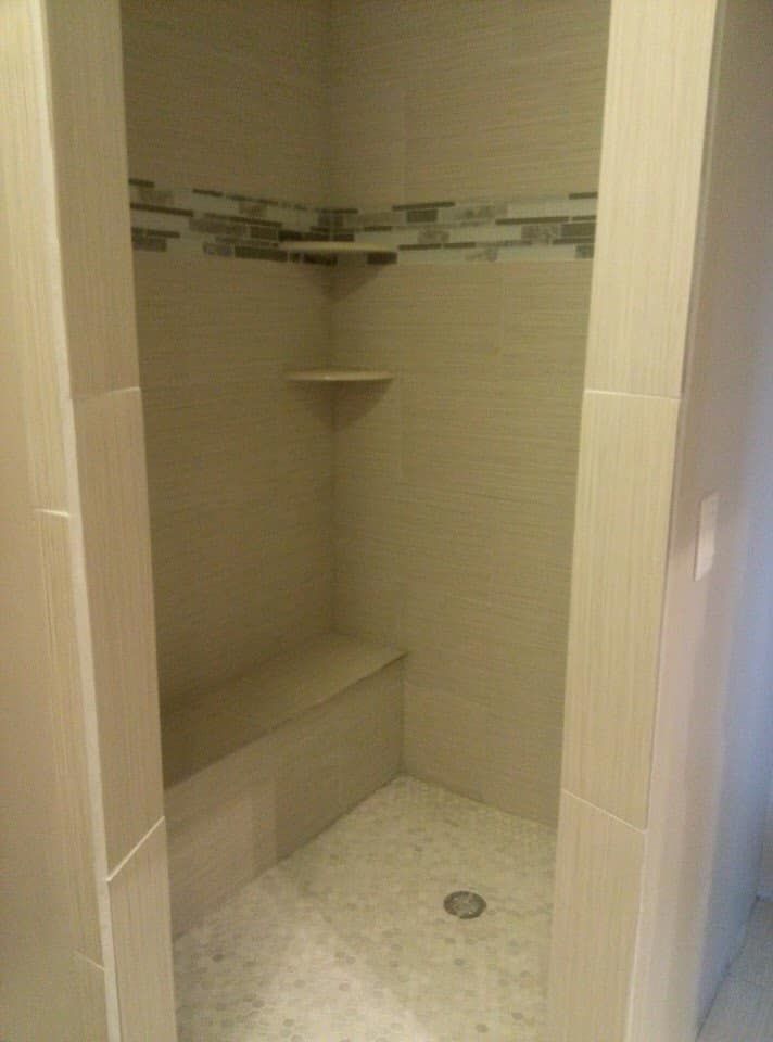Tiled shower with a built-in bench, two shelves, and a pebble tile floor. Beige and neutral colors.