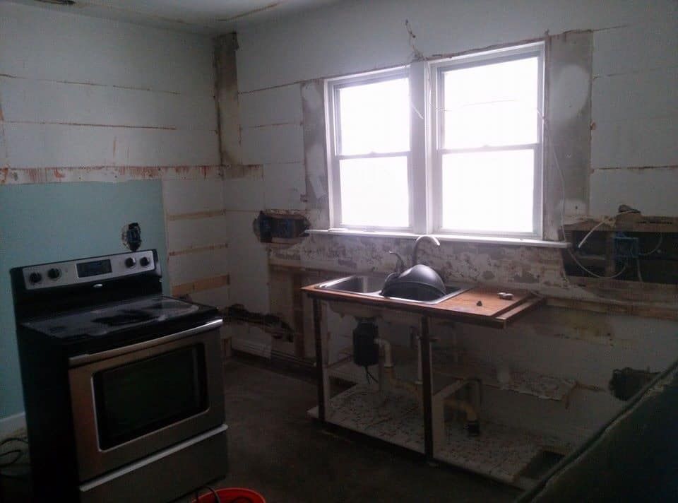 Kitchen remodel: Stainless steel oven on left, temporary sink under window, exposed wall studs.