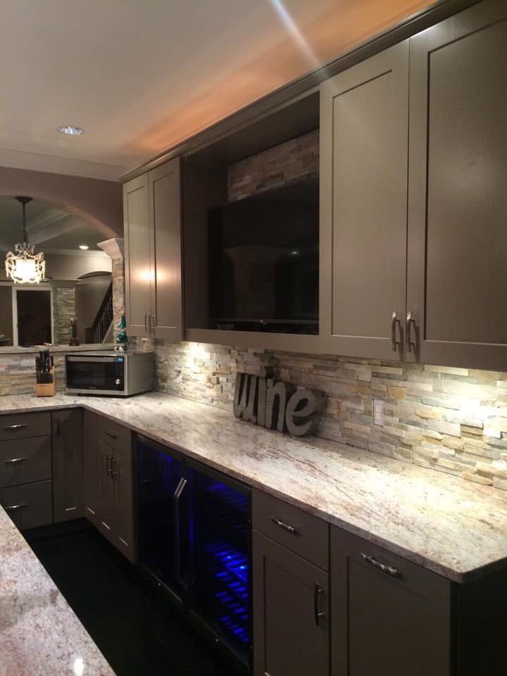 Modern kitchen with gray cabinets, granite countertops, built-in wine cooler, and TV above countertop.