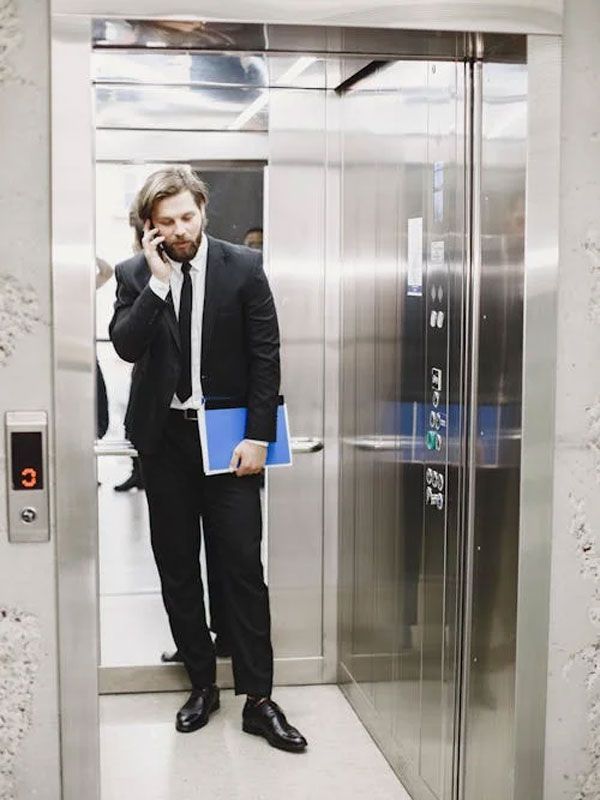 A man in a suit standing in a lift while using his mobile phone