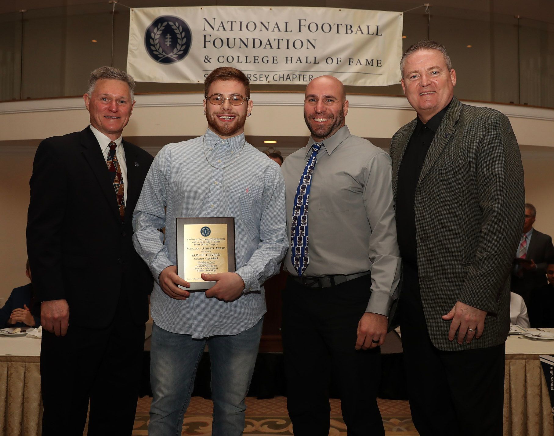 a group of men standing in front of a national football foundation banner