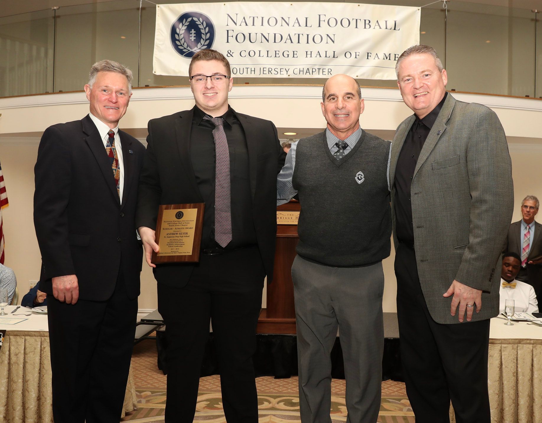 a group of men standing in front of a national football foundation banner
