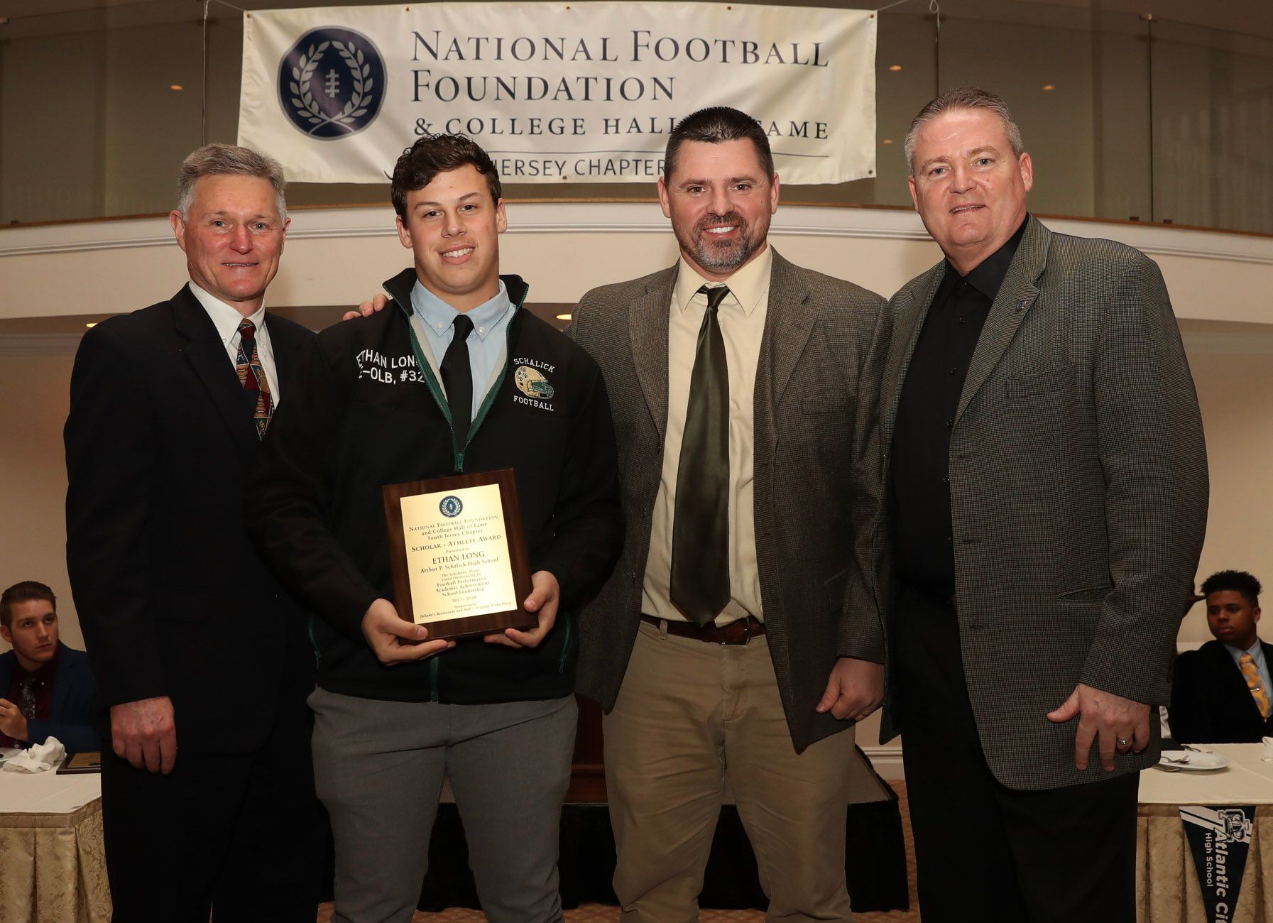 a group of men standing in front of a national football foundation banner