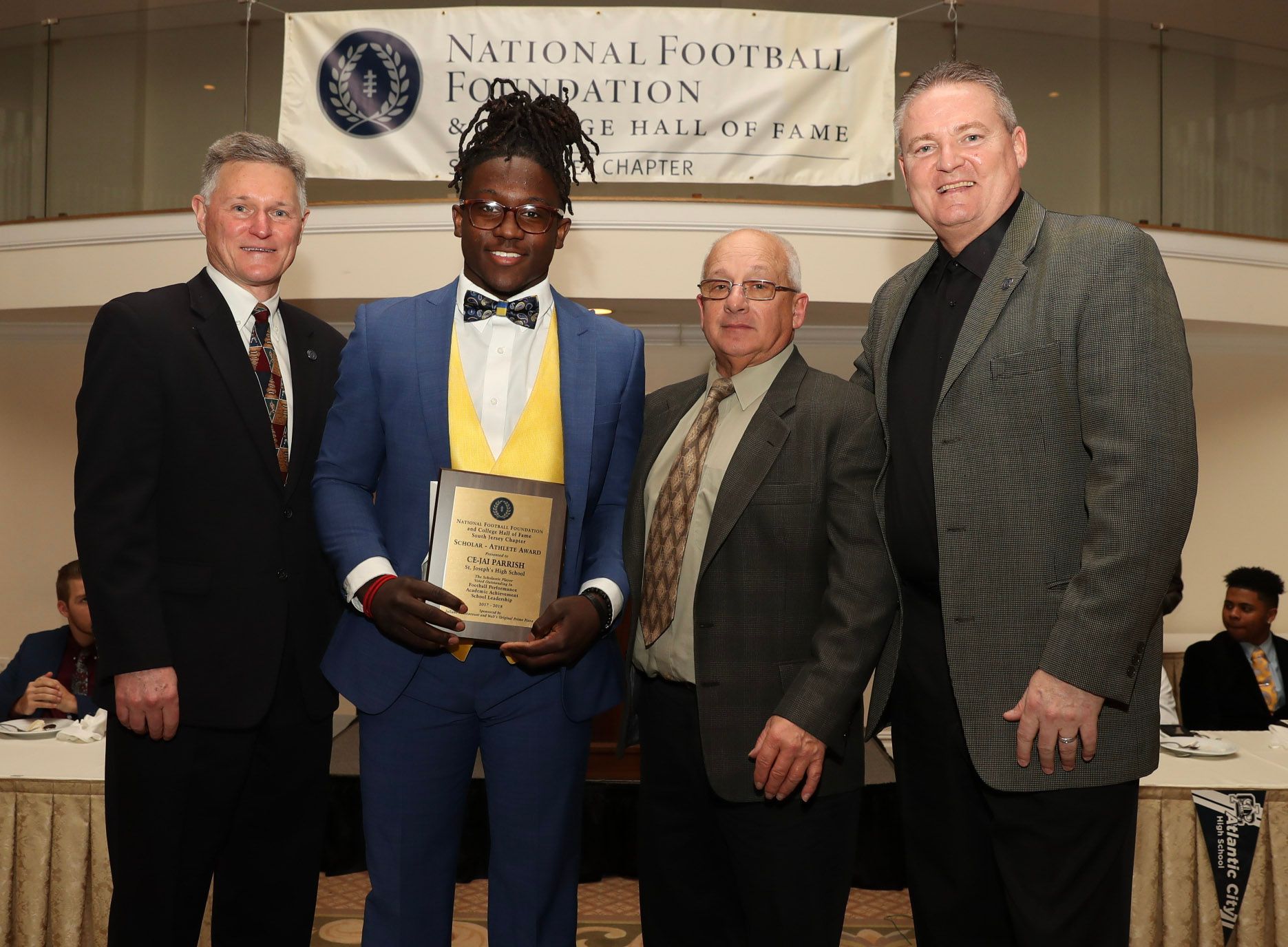 a man in a blue suit holds a plaque in front of a national football foundation banner