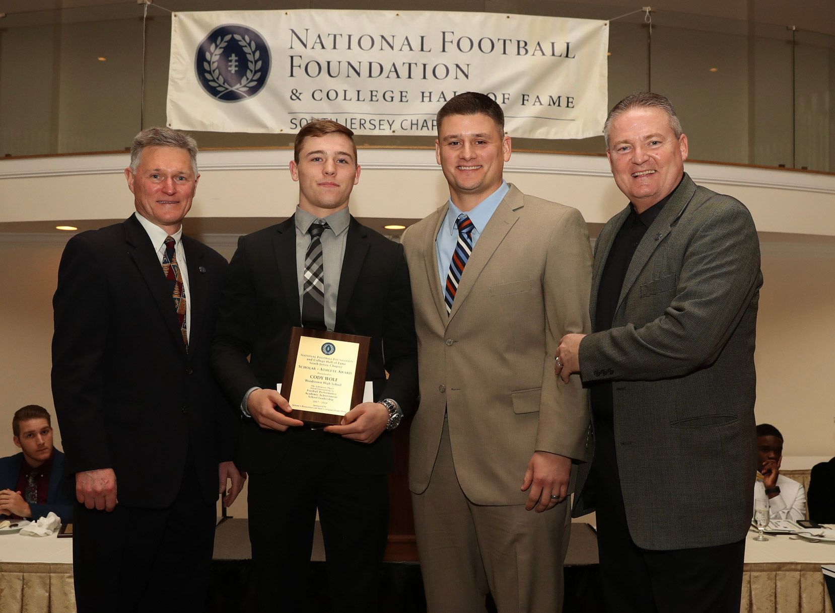 four men are posing for a picture in front of a national football foundation banner